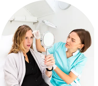 Healthcare professional performing a facial skin assessment while the patient looks into a handheld mirror